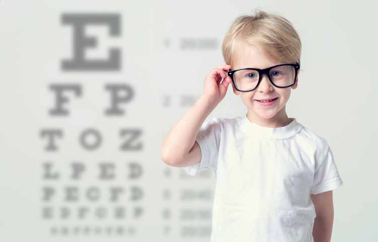 Little boy wearing eye glasses in front of an eye chart